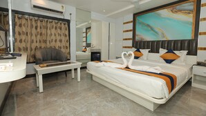 A hotel room with a bed, a desk, a chair, a ceiling fan, a large mirror, and a painting on the wall.