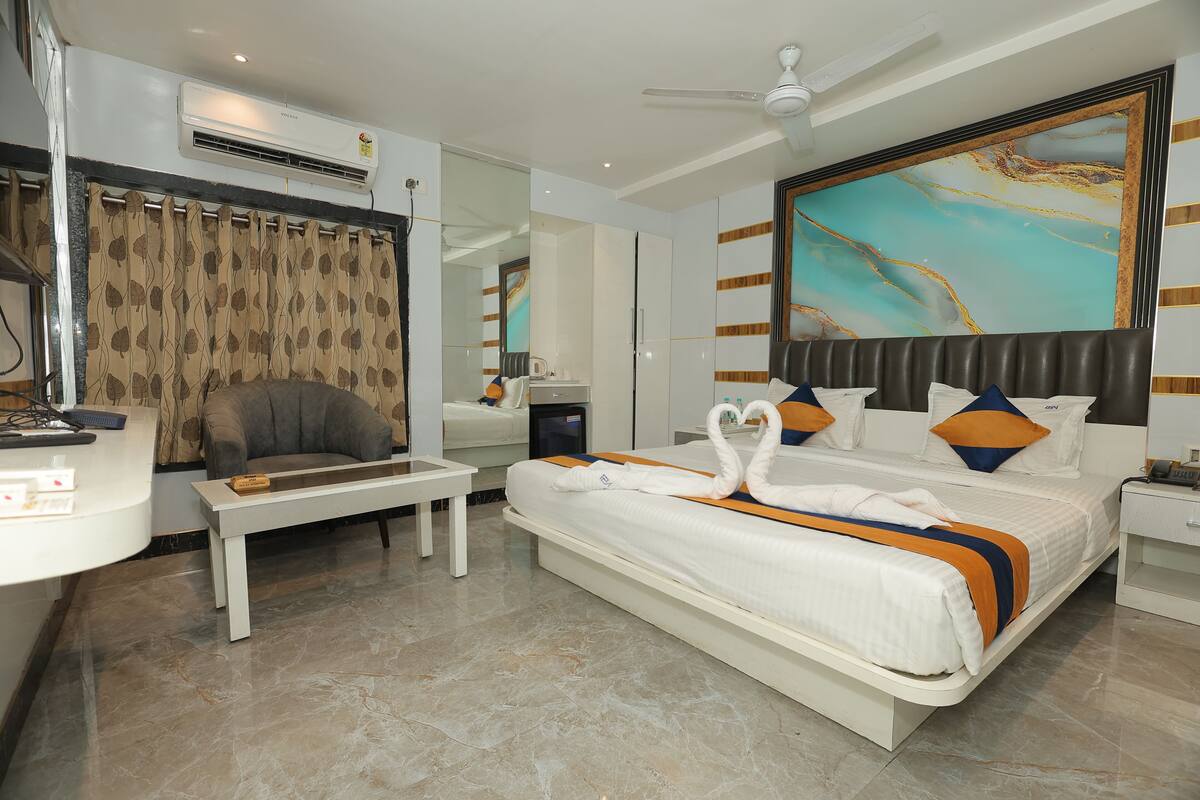 A hotel room with a bed, a desk, a chair, a ceiling fan, a large mirror, and a painting on the wall.