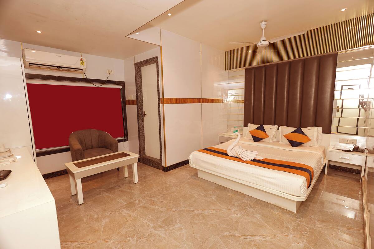 A hotel room with a bed, a chair, a desk, a mirror, and an air conditioning unit.