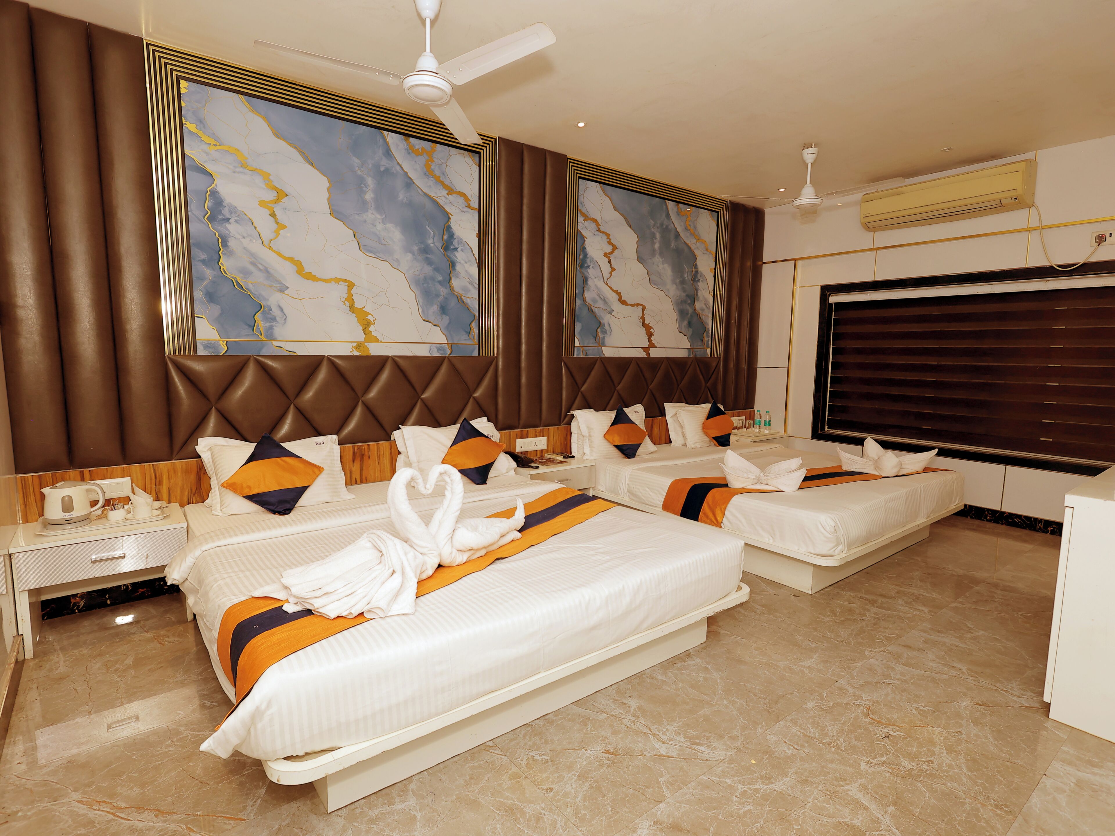 A hotel room with three beds, a large marble-patterned wall art, a ceiling fan, and an air conditioning unit.
