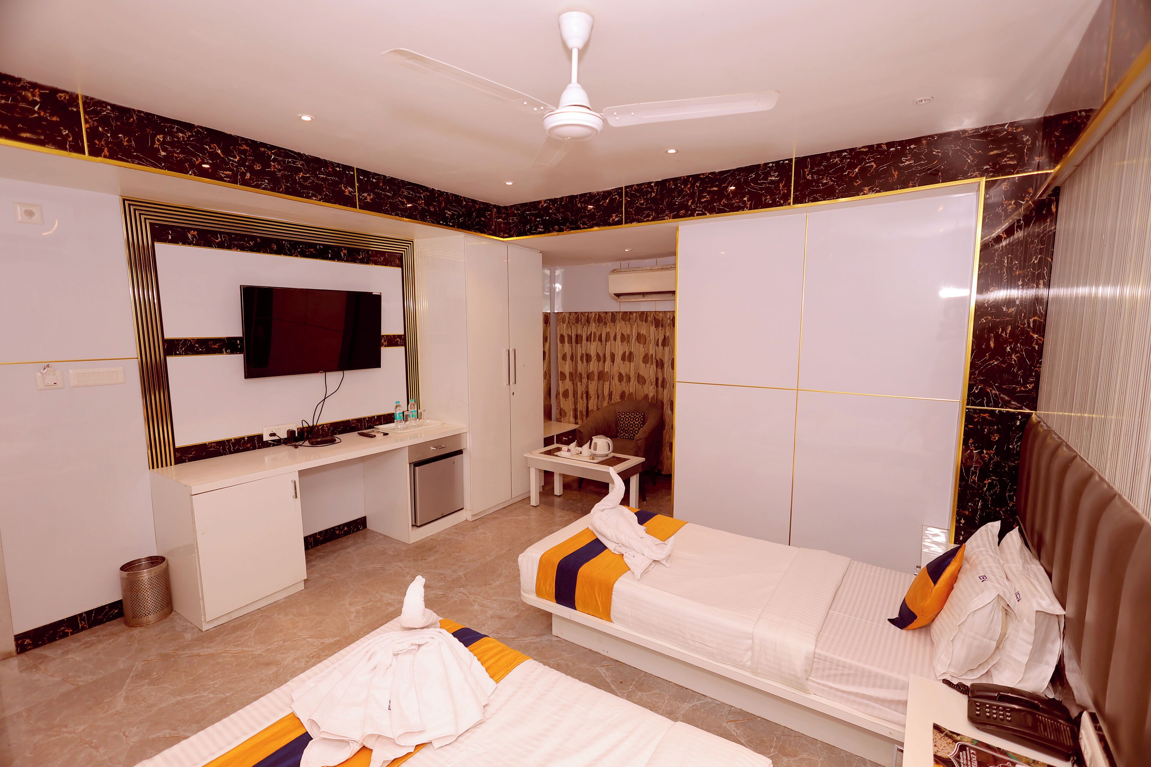 Habitación de hotel con cama, escritorio, televisor y ventilador de techo.
