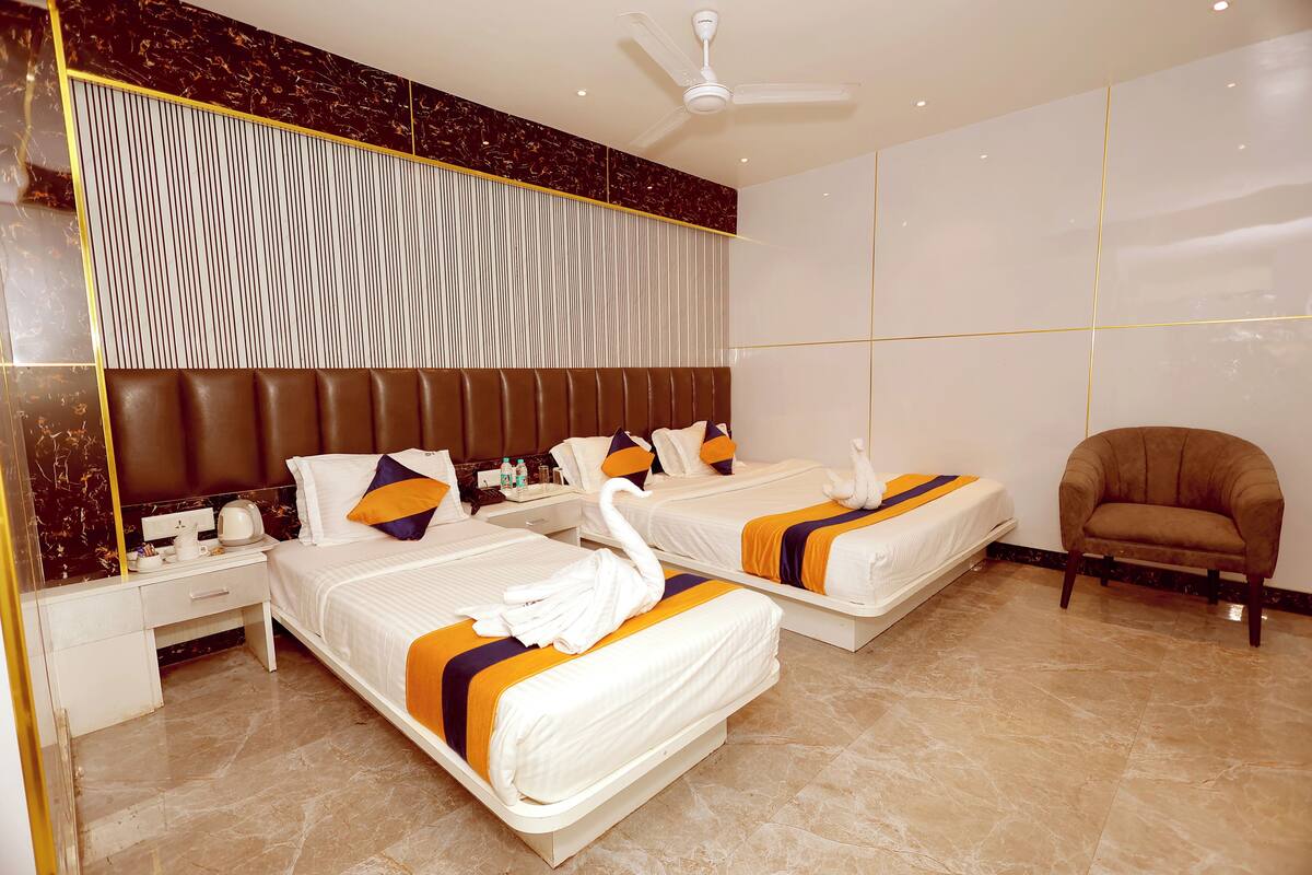 A hotel room with two beds, a sofa, a nightstand, and a ceiling fan.