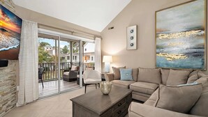 Una sala de estar con sofá, mesa de centro y sillón. Hay un ventanal corredero que da a un área exterior con patio.