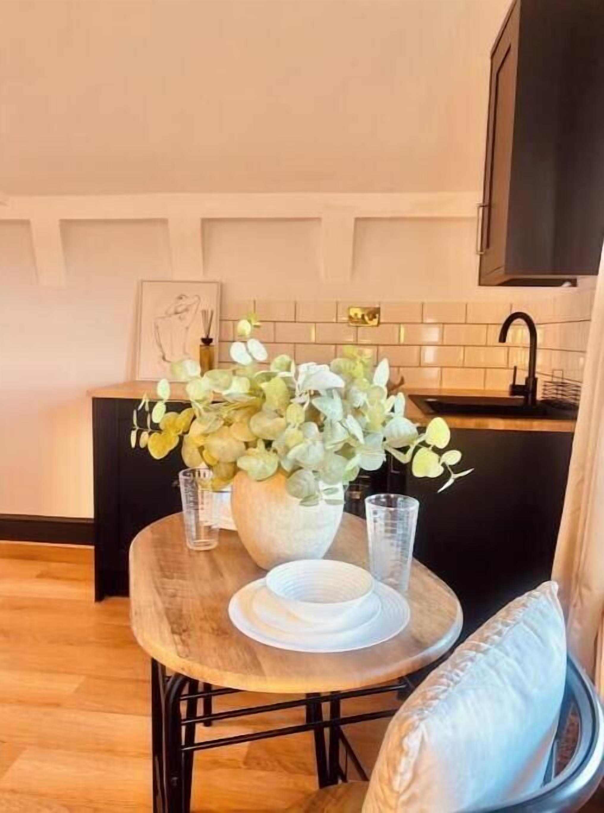Una cocina con una mesa redonda de madera, un jarrón con flores y una encimera negra.