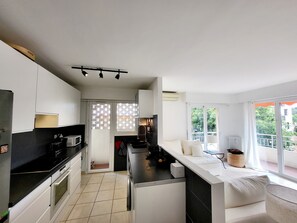 A modern kitchen with white cabinets, a black countertop, and a dining area with a white table and chairs. - Central Antibes, Spacious and Bright 2-Bedroom Apartment Near Beaches (Antibes)