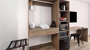 Una habitación moderna con escritorio integrado, televisor de pantalla plana, refrigerador compacto y una silla.
