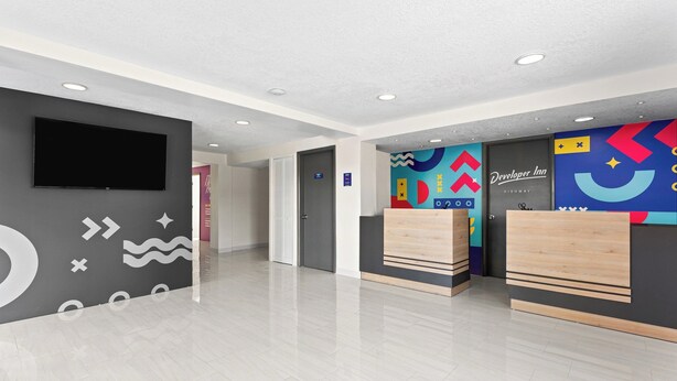 Un vestíbulo de hotel con un televisor de pantalla plana, una recepción y un mural de pared colorido.