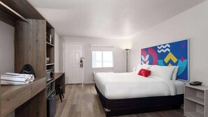 Un dormitorio con cama, escritorio, silla, armario y un cuadro abstracto colorido en la pared.