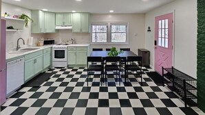 A compact kitchen with a checkered floor, a dining table with chairs, and a pink door. - Charming Pocono Bungalow with Firepit, Grill, Outdoor seating, Walk to Lake (Pocono Lake)