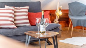 Eine Weinflasche auf einem Tisch mit zwei Gläsern, ein Sofa mit gestreiften Kissen und ein Sessel mit einer Lampe an der Wand.