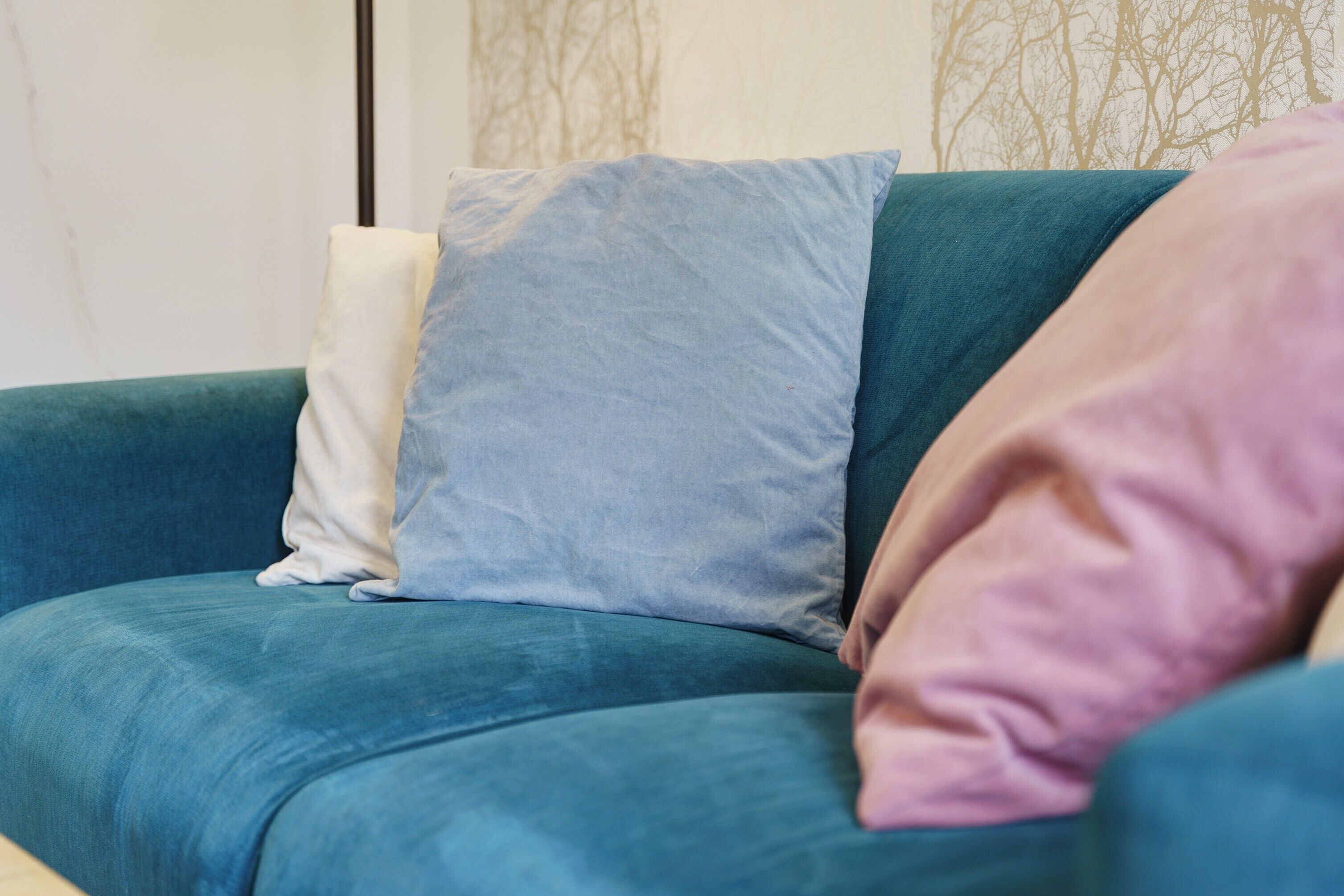 Ein hölzernes Sofa in Türkis mit drei Kissen in verschiedenen Farben.