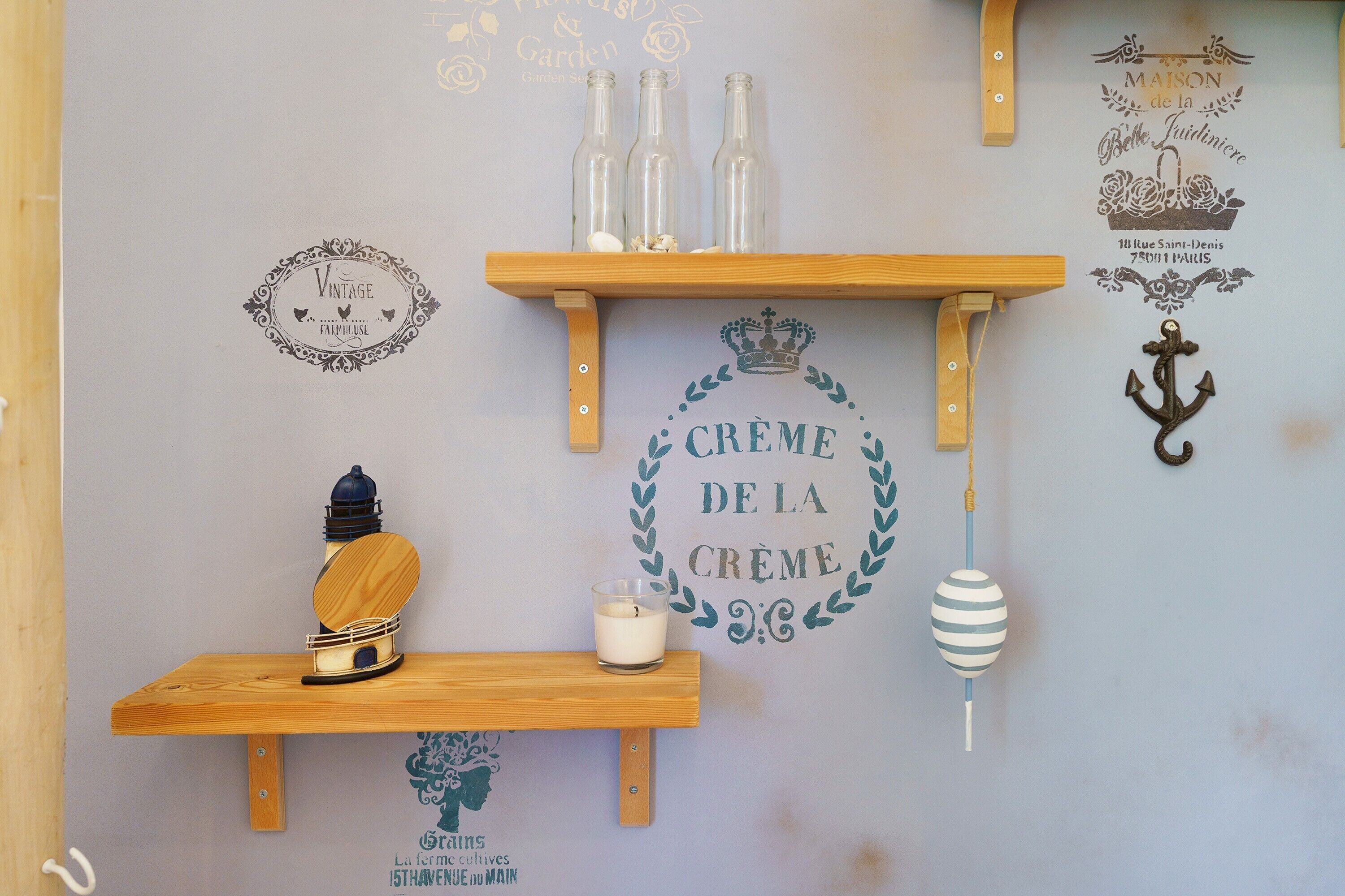 A wall with decorative wall art, including a vintage sign, a candle, and a small lamp on a shelf.