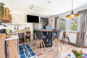 Een compacte keuken met moderne apparaten, een eethoek met stoelen, een aan de muur bevestigde televisie en een raam met gordijnen.