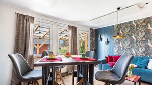 Ein modernes Wohnzimmer mit Esstisch, Stühlen, einer Couch und Blick auf eine Holzkonstruktion draußen.