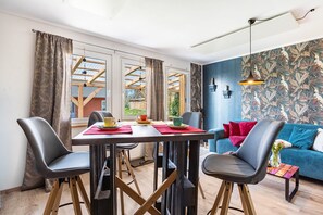 Een moderne woonkamer met een eettafel, stoelen, een bank en uitzicht op een houten constructie.