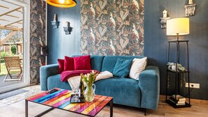 Ein Wohnzimmer mit einem türkisfarbenen Sofa, einem bunten Couchtisch, einer Lampe und einer gemusterten Tapete.