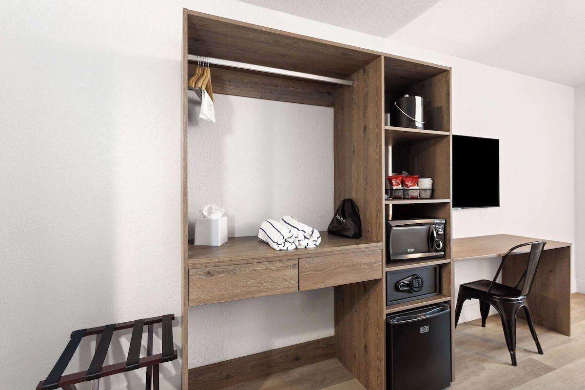 Una habitación moderna con escritorio integrado, televisor de pantalla plana, refrigerador compacto y una silla.