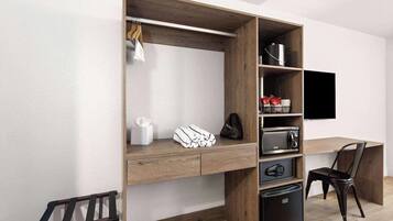 Una habitación moderna con escritorio integrado, televisor de pantalla plana, refrigerador compacto y una silla.