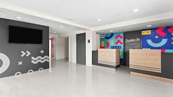 Un vestíbulo de hotel con un televisor de pantalla plana, una recepción y un mural de pared colorido.
