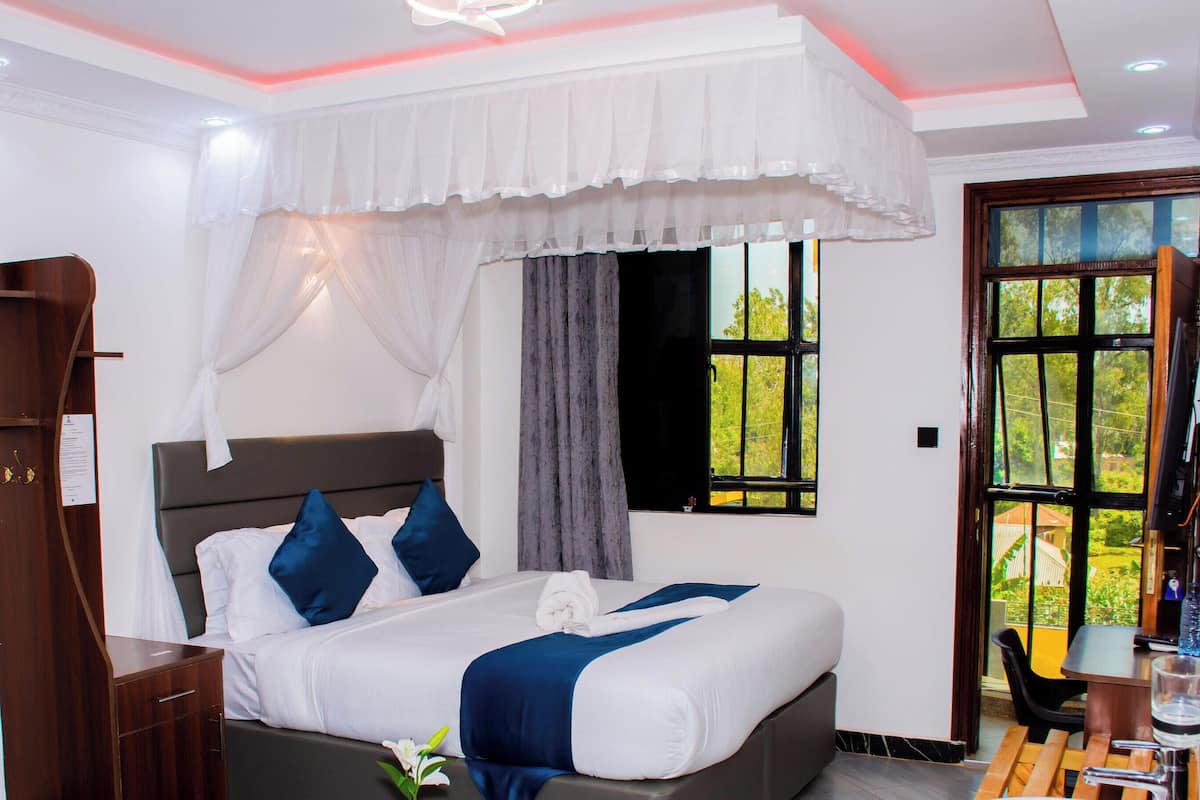 A bedroom with a bed, a nightstand, a wardrobe, a window with curtains, and a view of greenery outside.