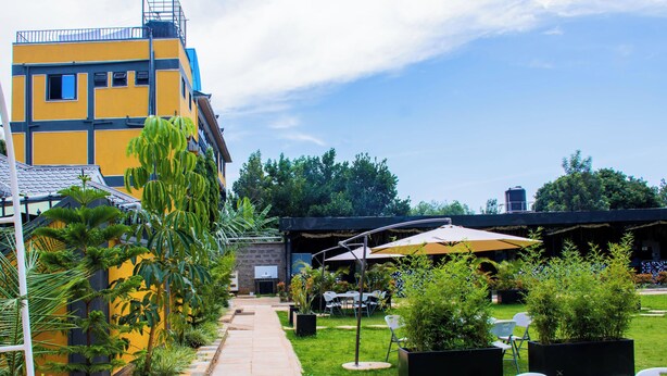 A courtyard with a yellow building, outdoor seating, and greenery. - The Grand Brystal Hotel (Busia)