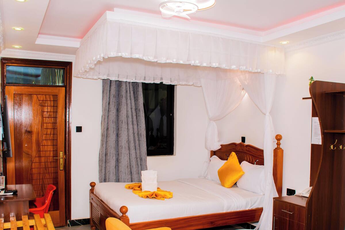 A bedroom with a wooden bed, a window with curtains, a bedside table, and a wardrobe.