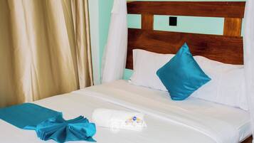 A bed with white bedding, a teal throw blanket, and a white towel with a logo.