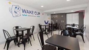 A breakfast cafe with black metal chairs and tables, a wall with a cartoon character and the text 'WAKE CUP BREAKFAST'. - 2 Queen | Howard Johnson | Room for Whole Crew! | Near Disney w/ Free Shuttle (Kissimmee)