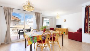 A dining area with a table and chairs, a television, a sofa, and a view through the glass door. - Sea, Sun & Relax in Alcalá (Guía de Isora)