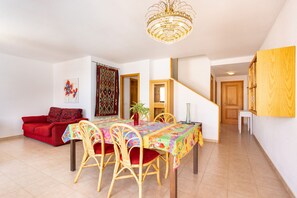 Ein Essbereich mit Tisch, Stühlen, einer Chandelüster, einem roten Sofa und einer Treppe.