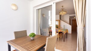 A dining area with a wooden table, wicker chairs, a potted plant, and a sliding glass door leading to a dining room. - Sea, Sun & Relax in Alcalá (Guía de Isora)