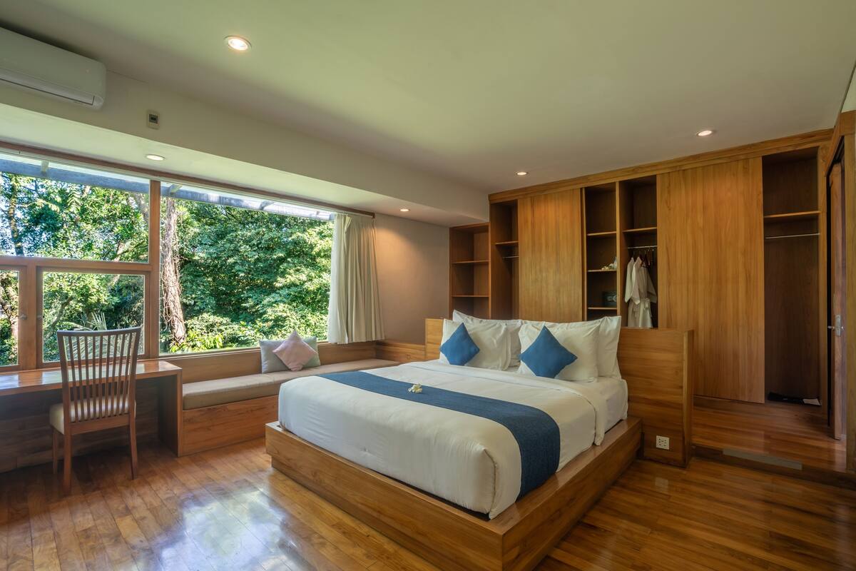A modern bedroom with a large bed, built-in wardrobe, and a seating area by a window.