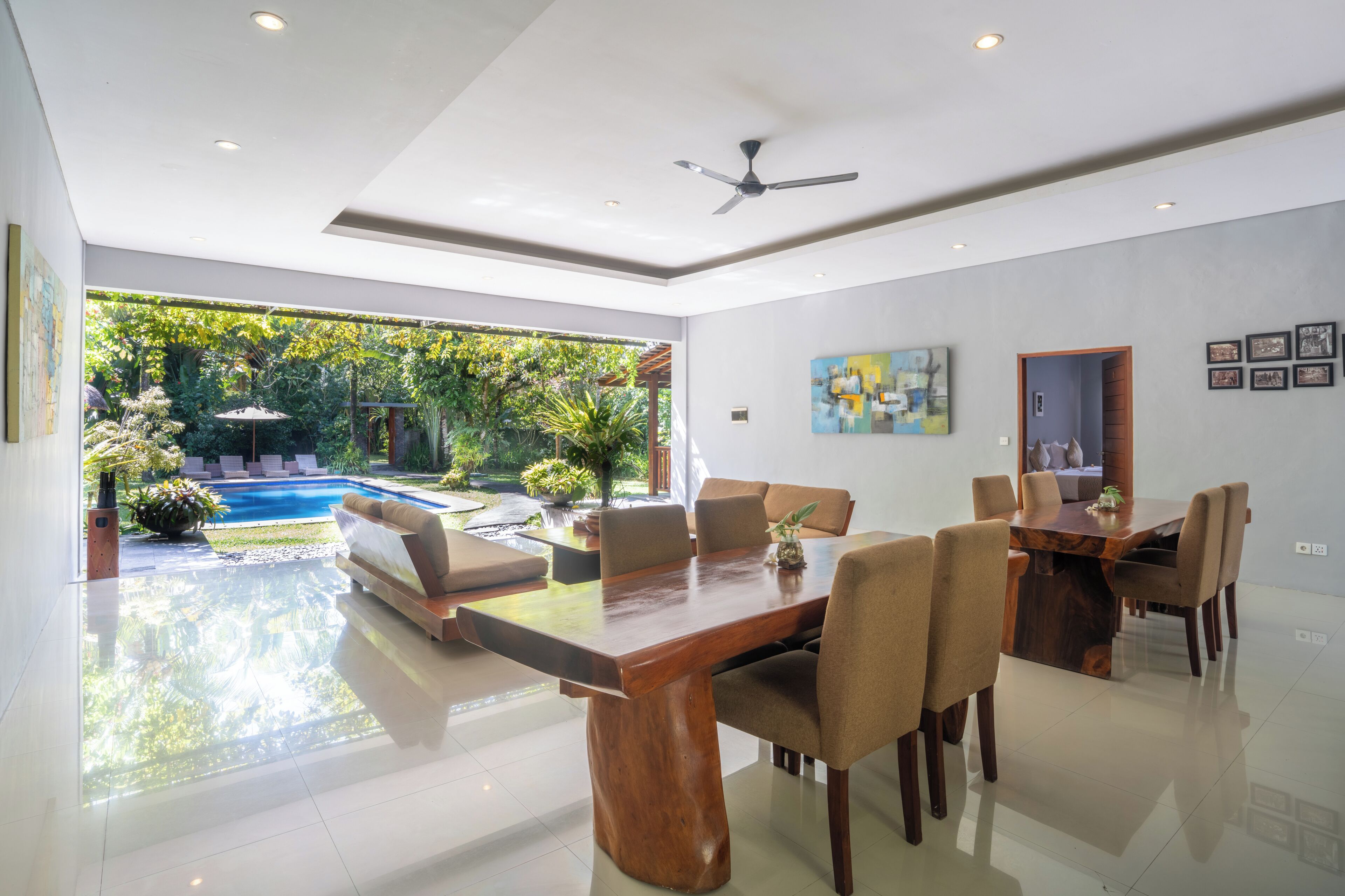 A modern dining area with a wooden table and chairs, a ceiling fan, and a view of a swimming pool and garden.