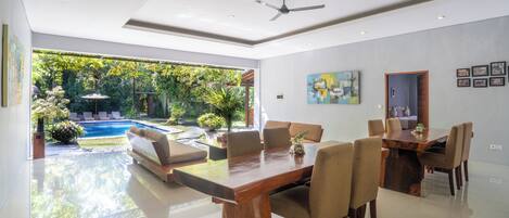 A modern dining area with a wooden table and chairs, a ceiling fan, and a view of a swimming pool and garden.