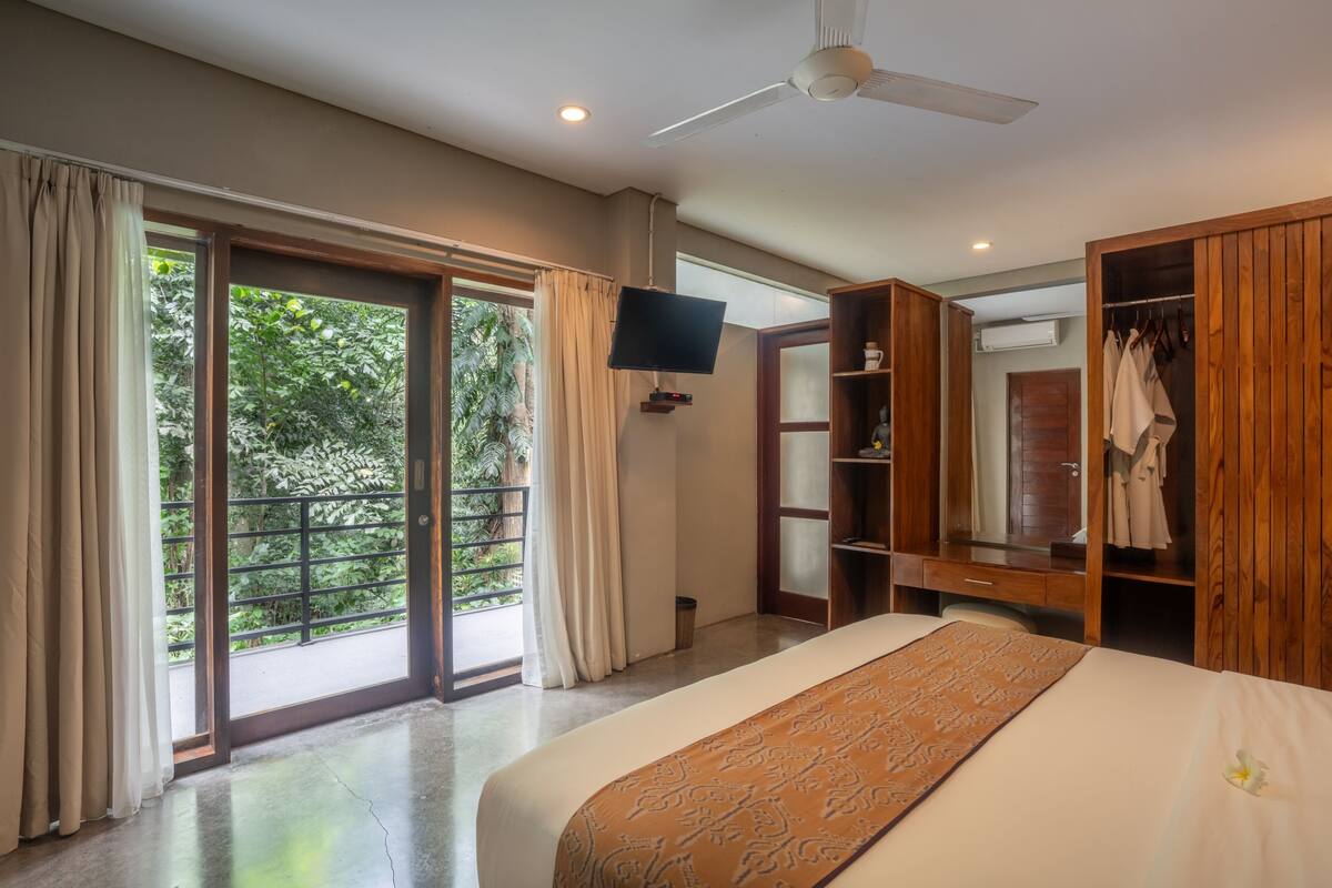 A bedroom with a bed, a TV, a wardrobe, and a balcony with curtains.