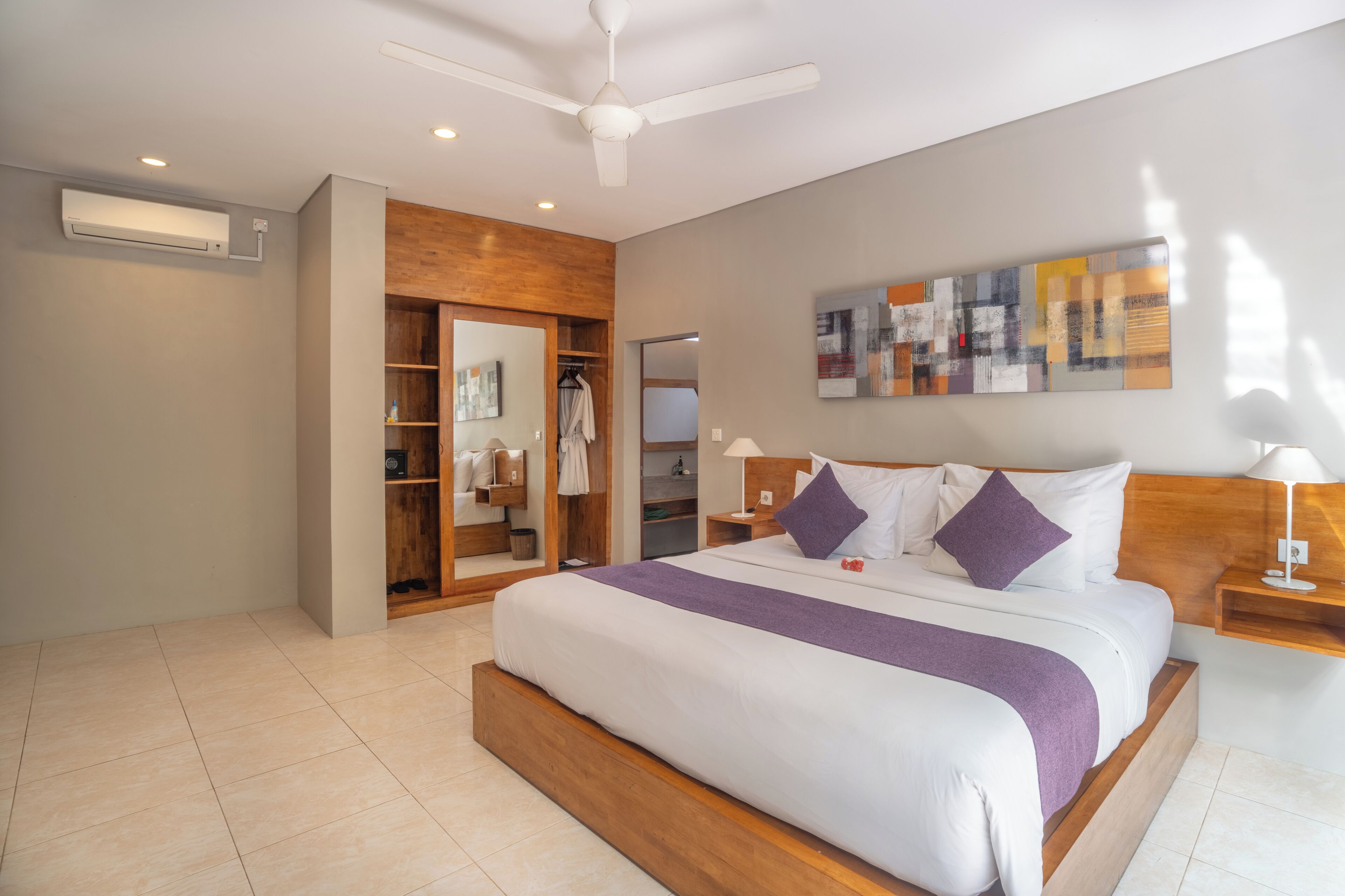 A modern hotel room with a large bed, a ceiling fan, a wardrobe, and a wall-mounted artwork.