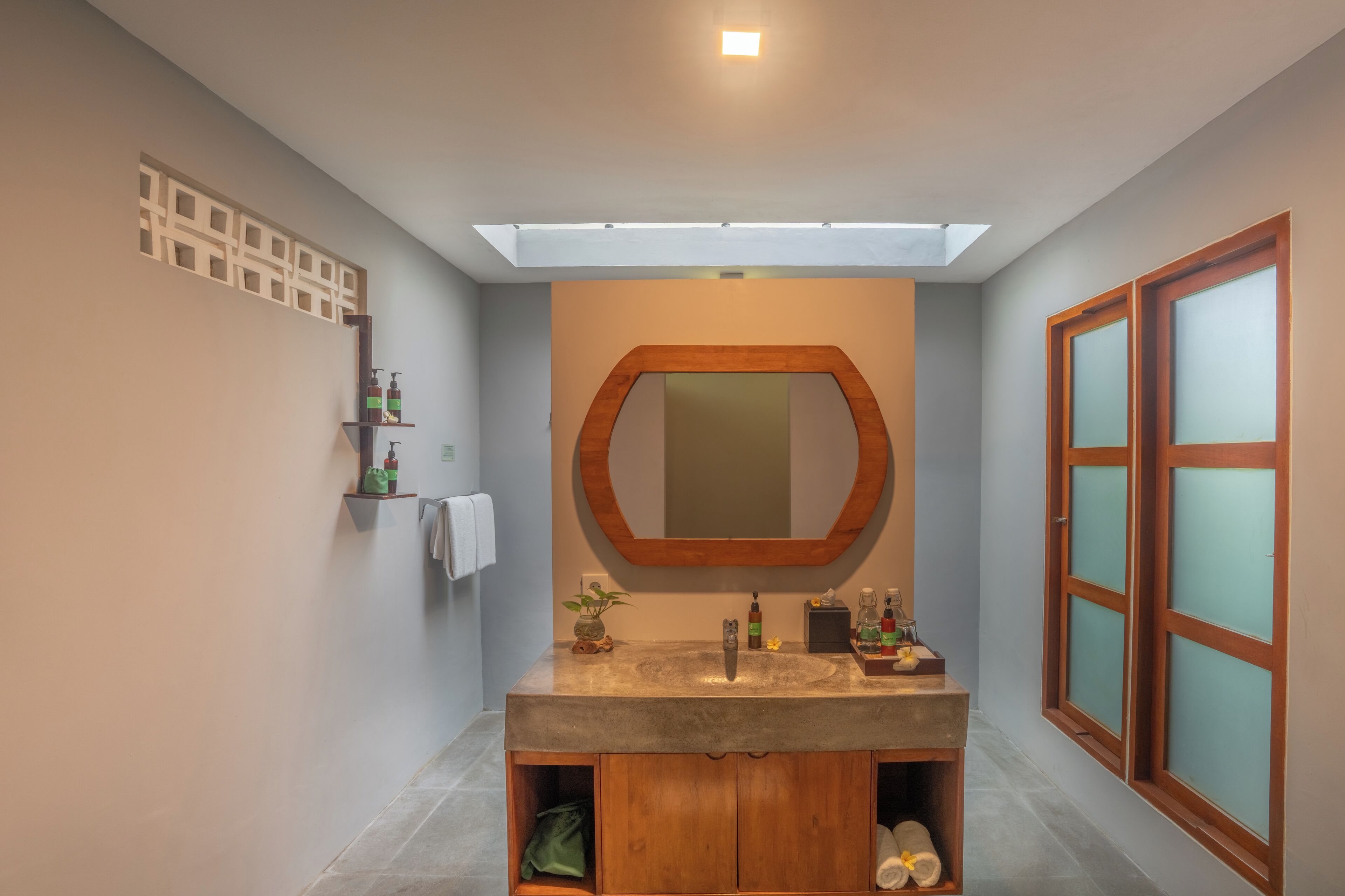 A modern bathroom with a skylight, a wooden vanity, a large mirror, and a window with frosted glass.
