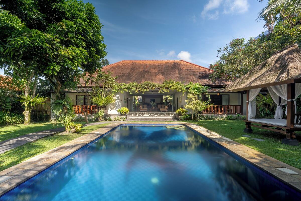 A swimming pool with a clear view of a building with a red roof and a thatched roof structure.