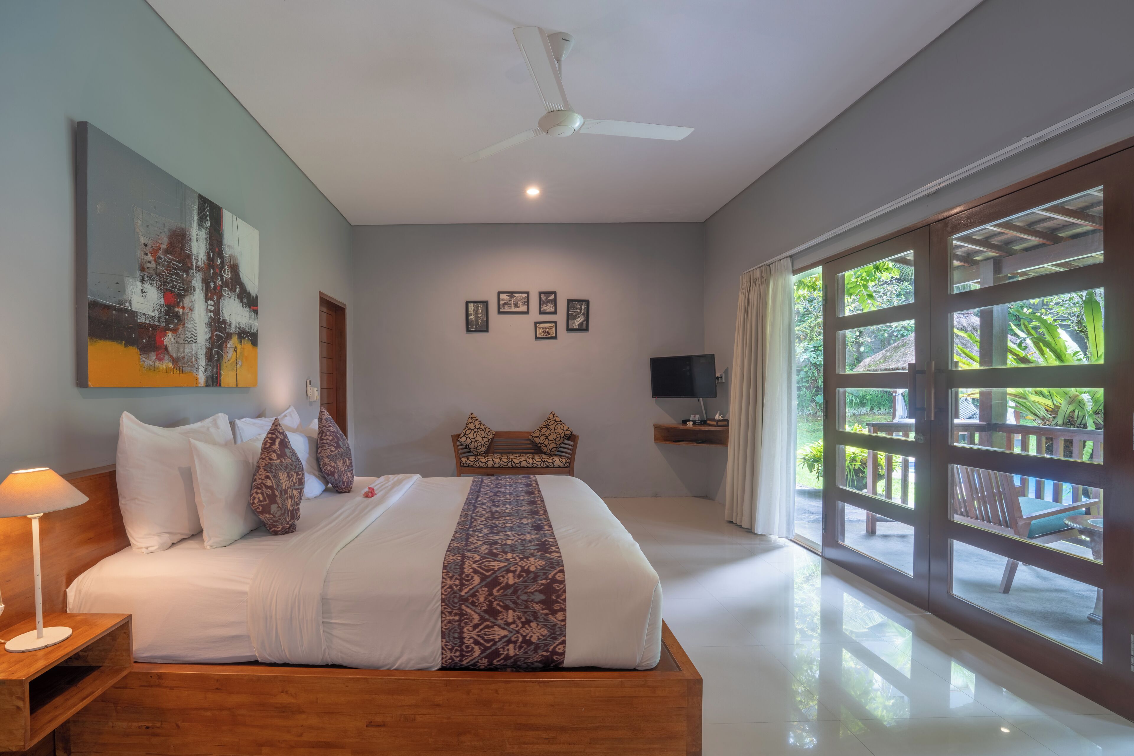 A bedroom with a bed, a ceiling fan, a TV, and a large window.