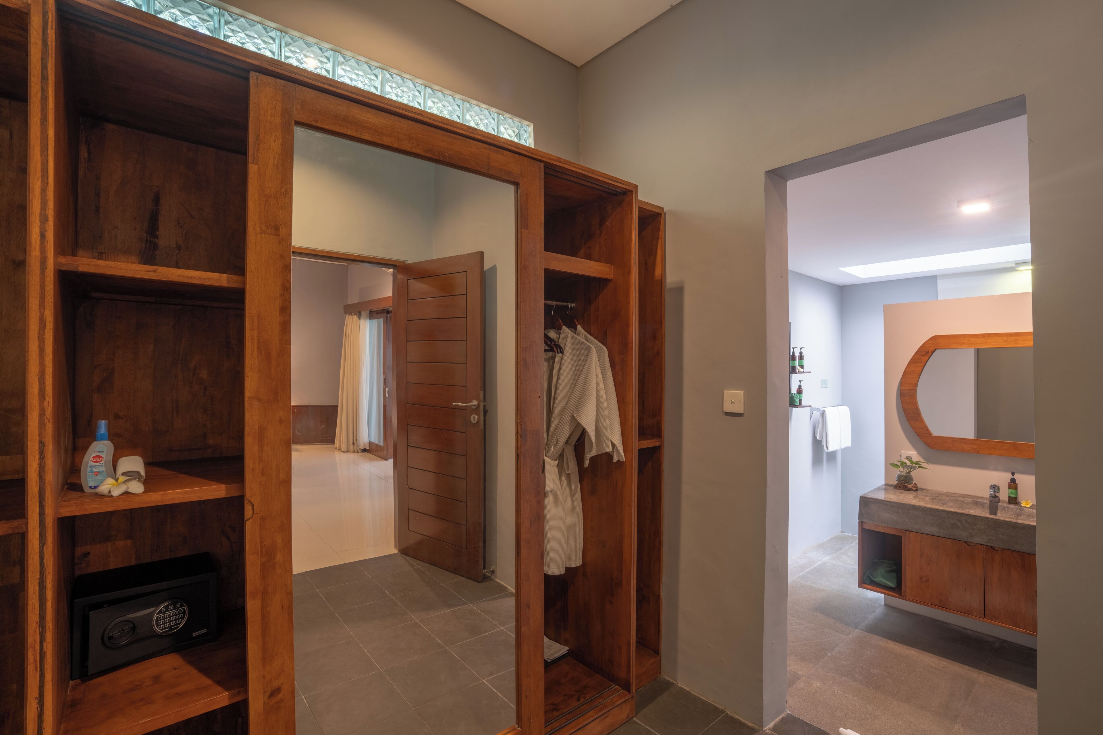 A modern bathroom with a wooden vanity, a large mirror, and a walk-in closet with shelves.