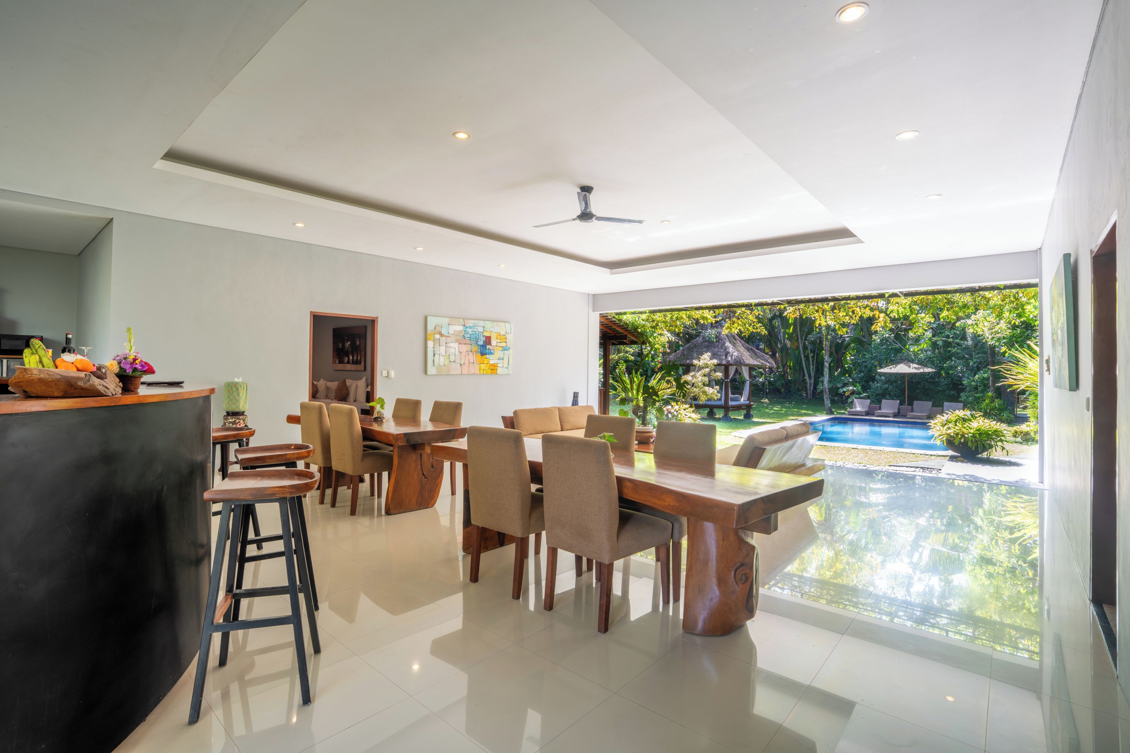 A modern dining area with a pool view, a bar, and a ceiling fan.