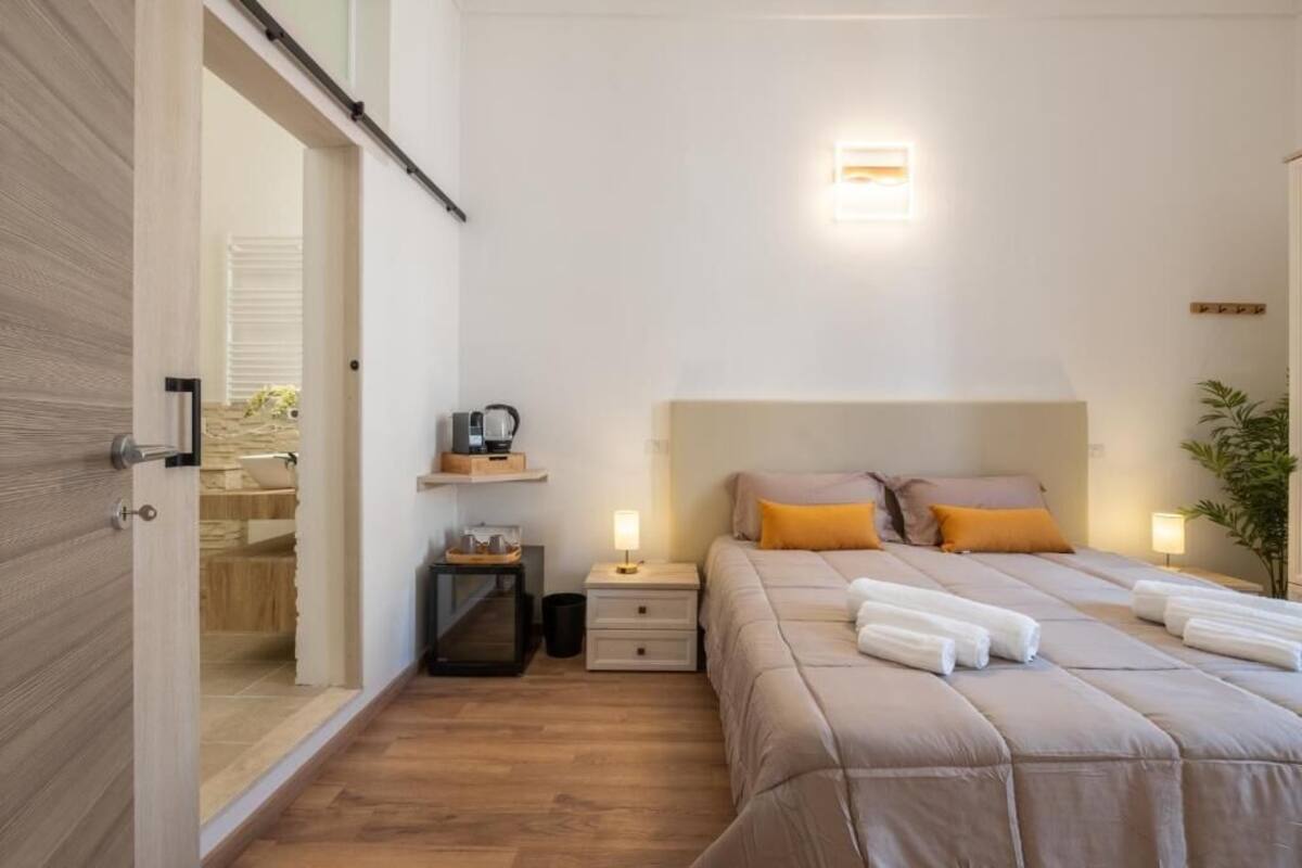 Ein Schlafzimmer mit Bett, Nachttischen, einer Wandleuchte und einer Tür zu einem Badezimmer.