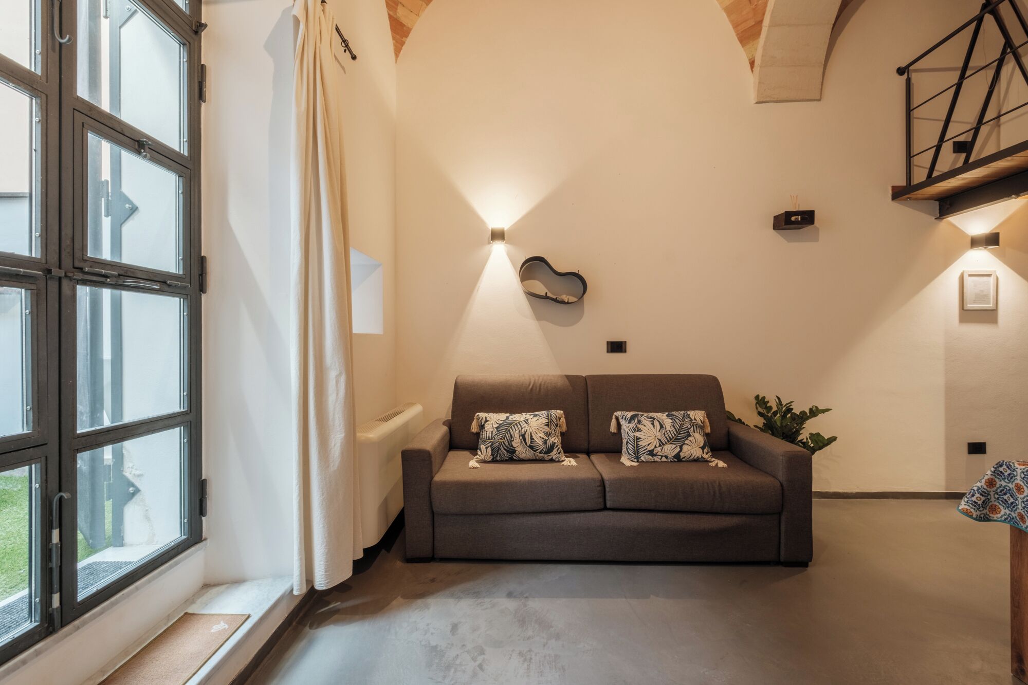 Una habitación con sofá, radiador, una guitarra colgada en la pared y una escalera.