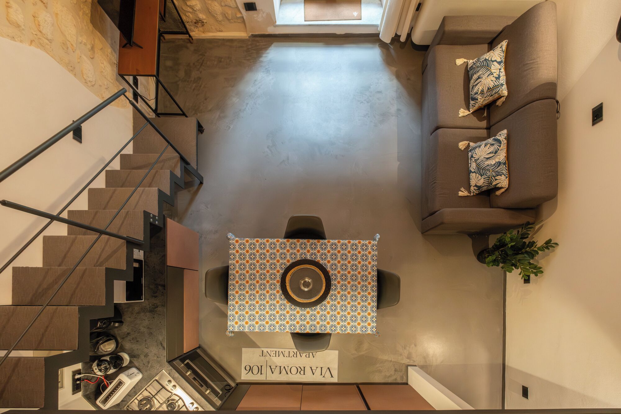 Amplia sala de estar con techo alto, una escalera, un sofá con cojines estampados y una mesa con un centro decorativo.