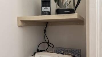 Una kitchenette con cafetera, hervidor de agua y una bandeja de cápsulas de café.