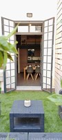 Un patio con mesa y sillas, un pequeño jardín y vistas a un comedor con otra mesa y sillas.