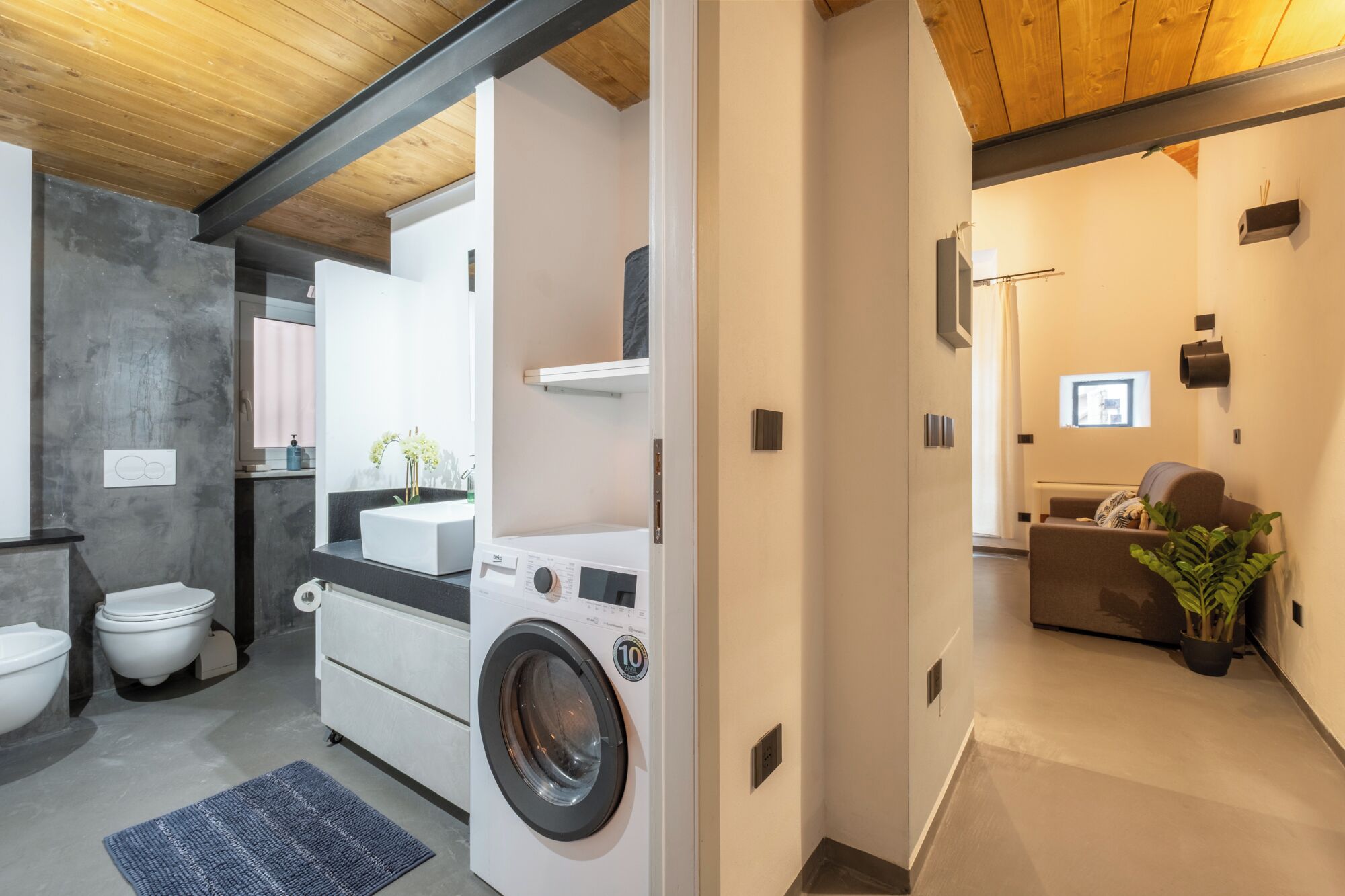 A compact, modern bathroom with a built-in washing machine, a toilet, and a sink.