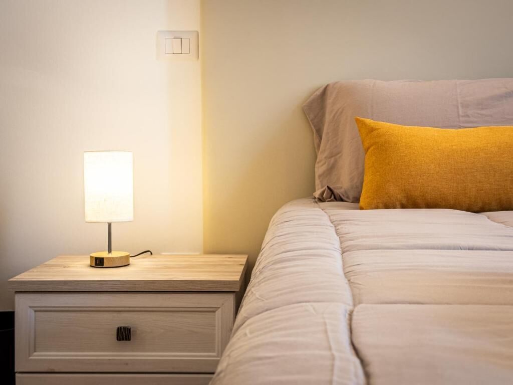 Una cama bien hecha con un edredón de color claro y una almohada amarilla.
