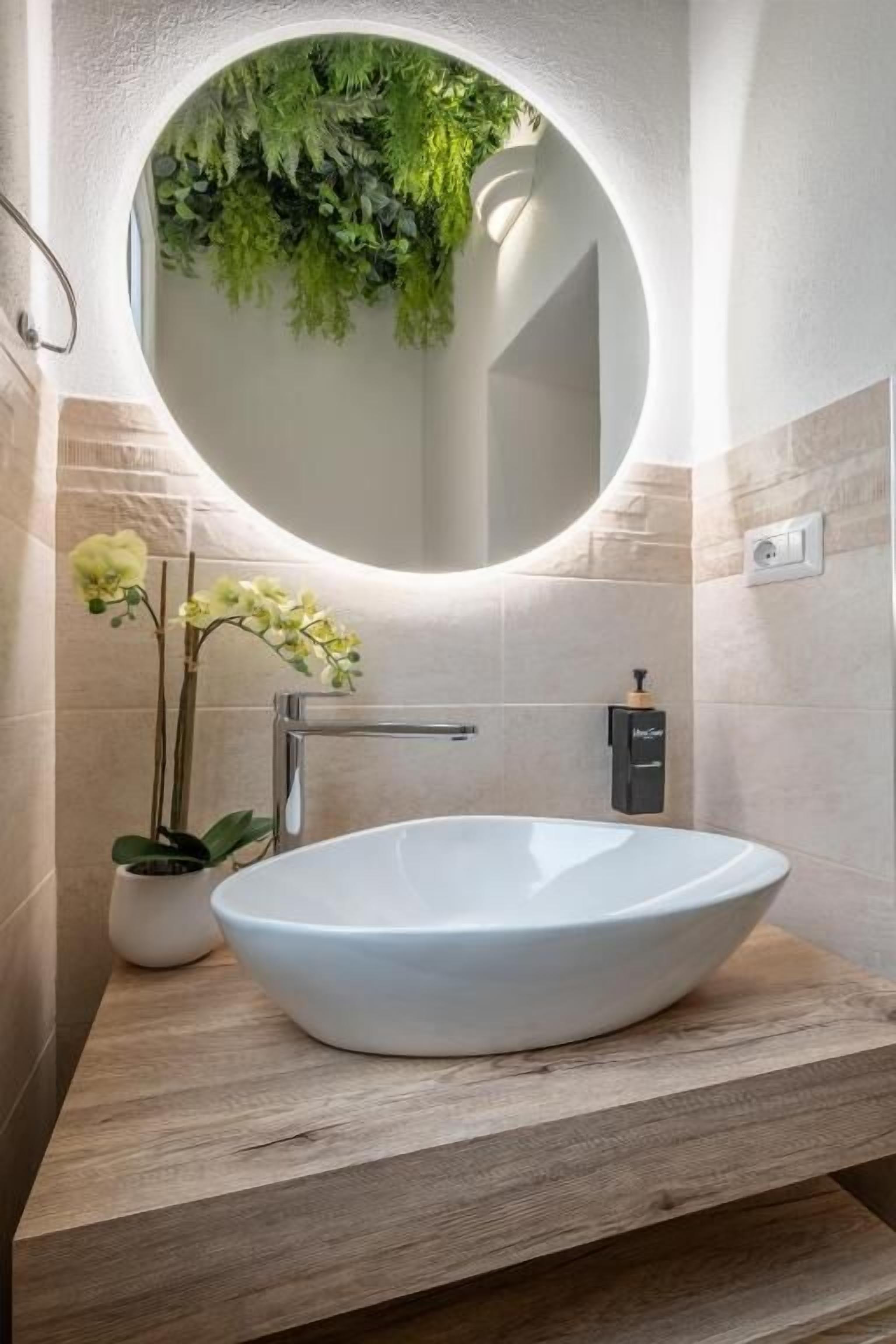 A modern bathroom with a round mirror, white sink, and a potted orchid.