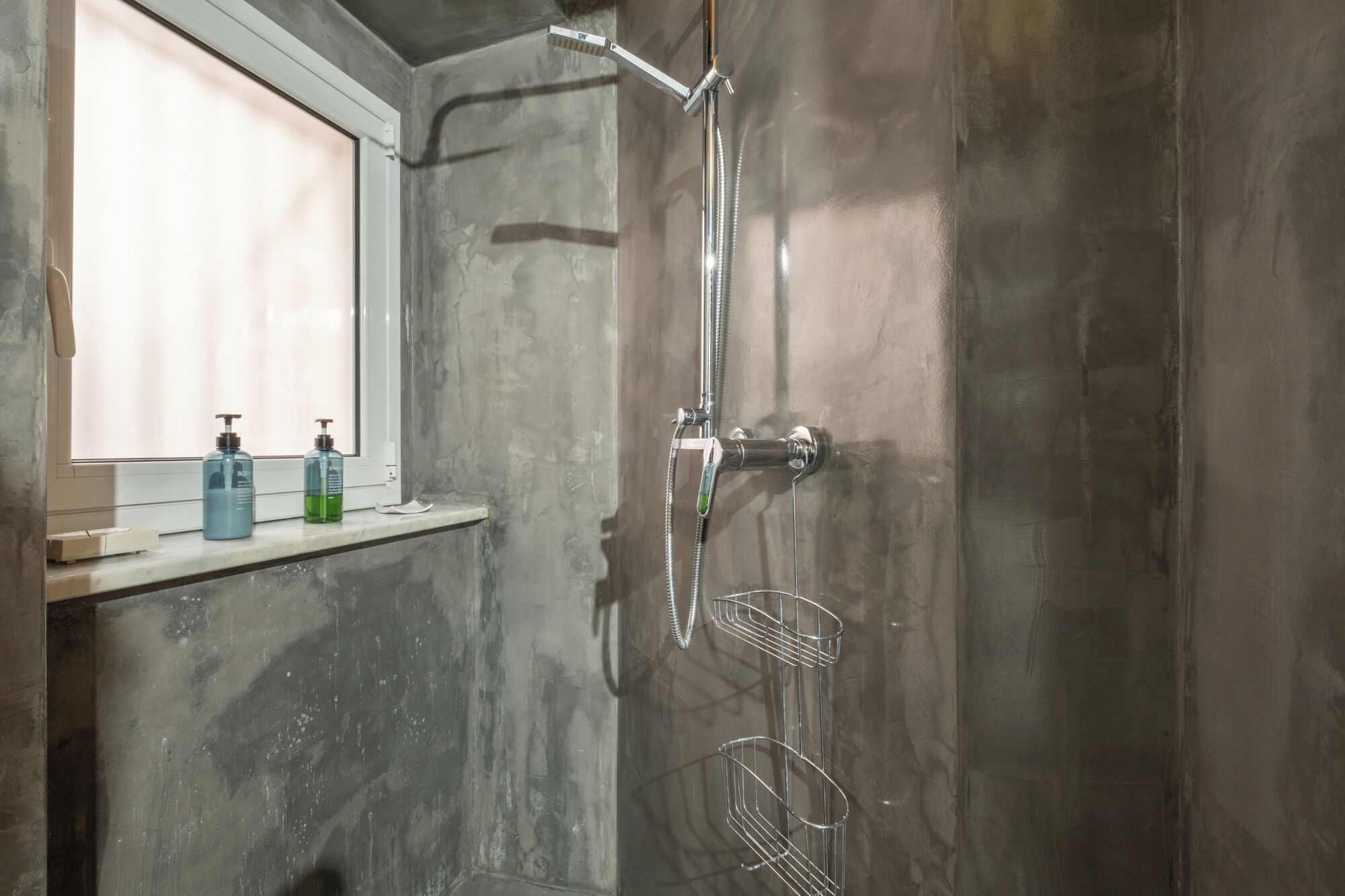 A shower with a handheld showerhead, a wall-mounted faucet, and a metal rack.